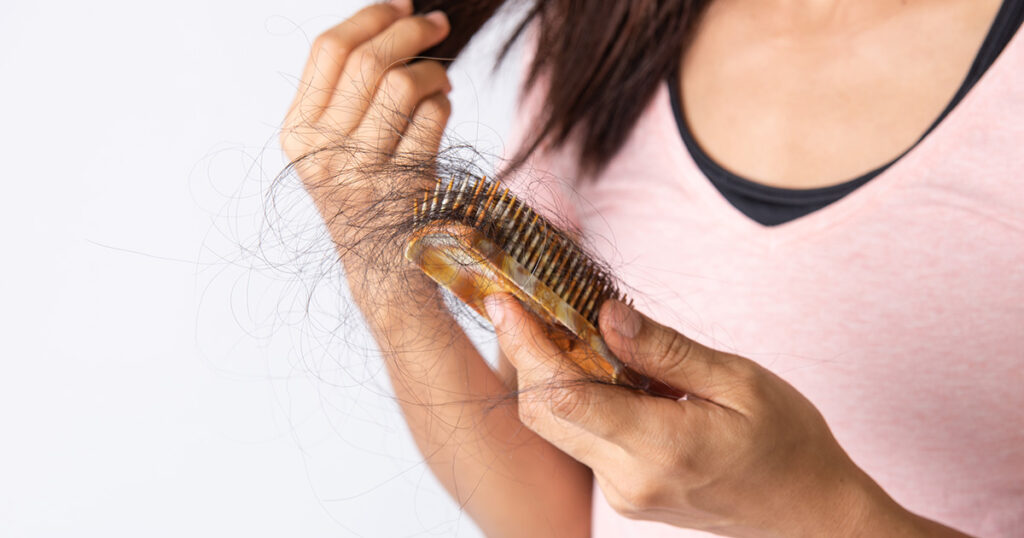 Woman holding a hairbrush full of fallen hair, indicating excessive hair loss and possible underlying health or lifestyle issues.